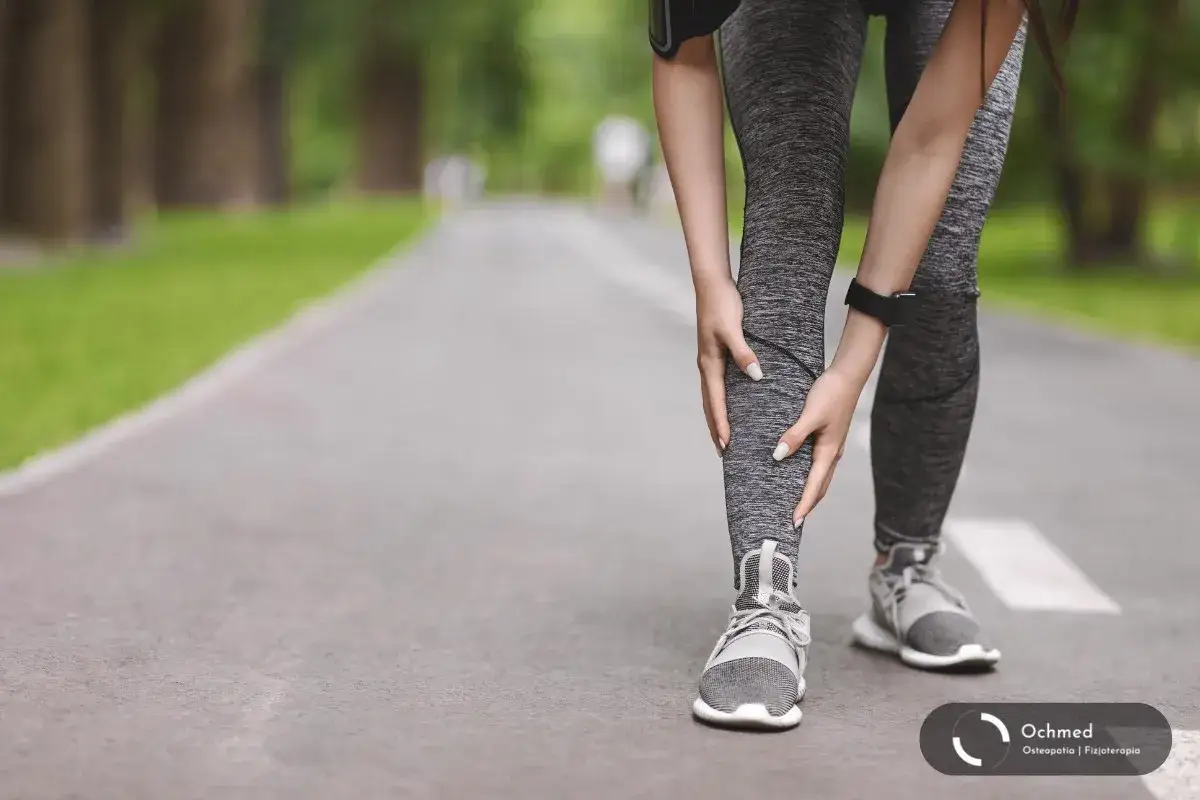 Biegaczka trzyma się za łydkę, odczuwając ból związany z zapaleniem okostnej (shin splints).