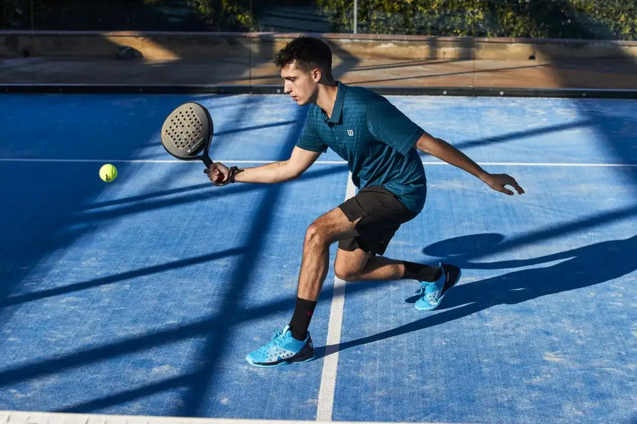 Młody mężczyzna gra w padla, odbijając piłkę rakietą. Poznaj padel zasady i zasady gry na korcie.