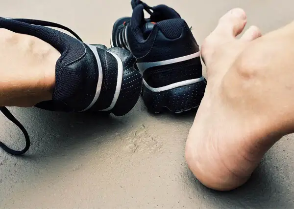 Czarne buty sportowe i bosa stopa na ziemi. Czas na trening, nawet jeśli paznokcie biegacza dają o sobie znać.