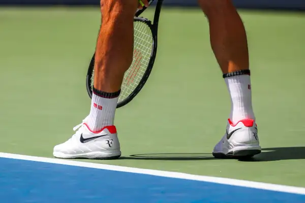Widok na łydkę tenisisty w białych skarpetkach i butach Nike, gotowego do uderzenia.