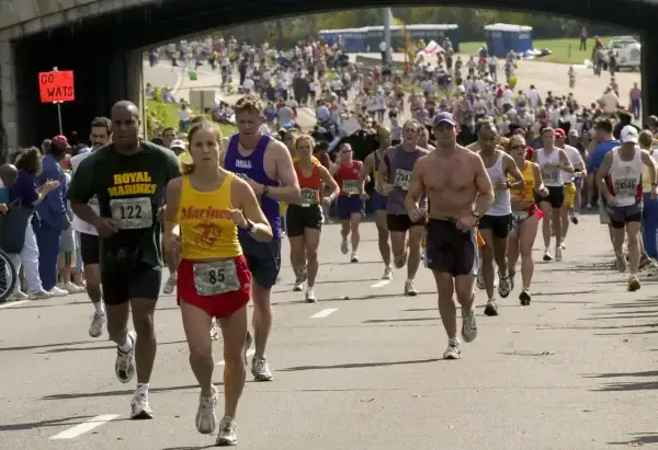 Uczestnicy biegną w maratonie, zastanawiając się, ile trwa maraton. Widać zawodników z numerami startowymi, kibiców i most nad trasą.