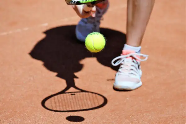Tenisista przygotowuje się do uderzenia piłki. Cień rakiety i piłki na korcie przypomina, co to ATP.