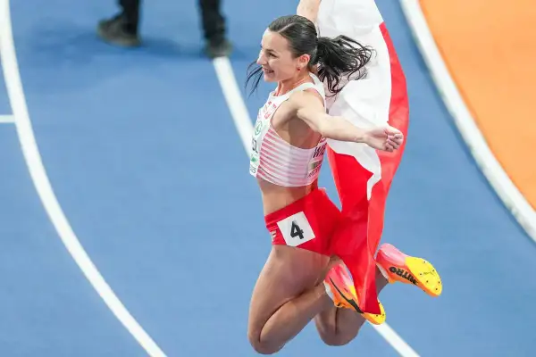 Polska biegaczka w skoku radości, z biało-czerwoną flagą. Numer 4 na spodenkach.