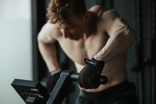 Mężczyzna w rękawiczkach ćwiczy cardio na rowerze stacjonarnym, skupiony na treningu.