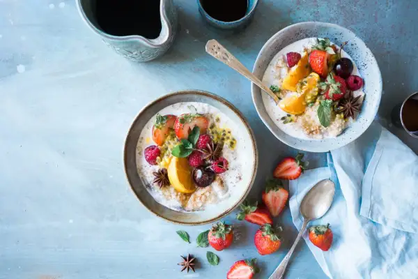 Dwa talerze owsianki z owocami (truskawki, maliny, pomarańcza, marakuja) i gwiazdkami anyżu. Idealne na śniadanie w stylu dieta wysokowęglowodanowa.
