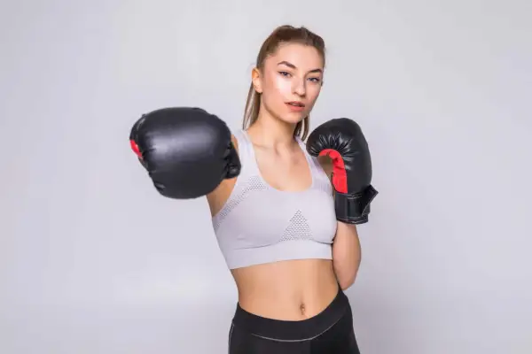 Młoda kobieta w sportowym topie i legginsach, w rękawicach bokserskich, ćwiczy w domu.