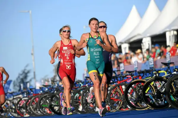 Trzy zawodniczki biegną w zawodach triathlonowych. To dyscyplina łącząca pływanie, jazdę na rowerze i bieg.