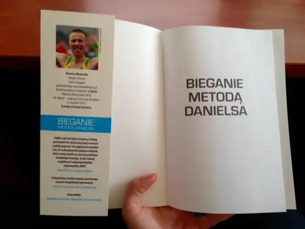 Otwarta książka z hasłem "Bieganie metodą Danielsa" na prawej stronie. Na lewej stronie zdjęcie biegacza i opis jego osiągnięć.